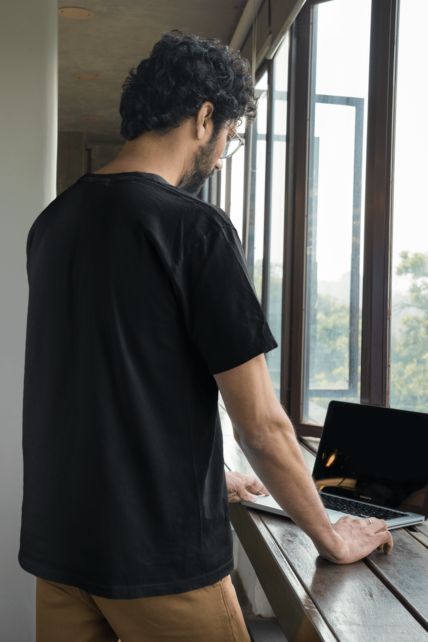 Man wearing a casual Black Tee-shirt in the office and working on a laptop.
