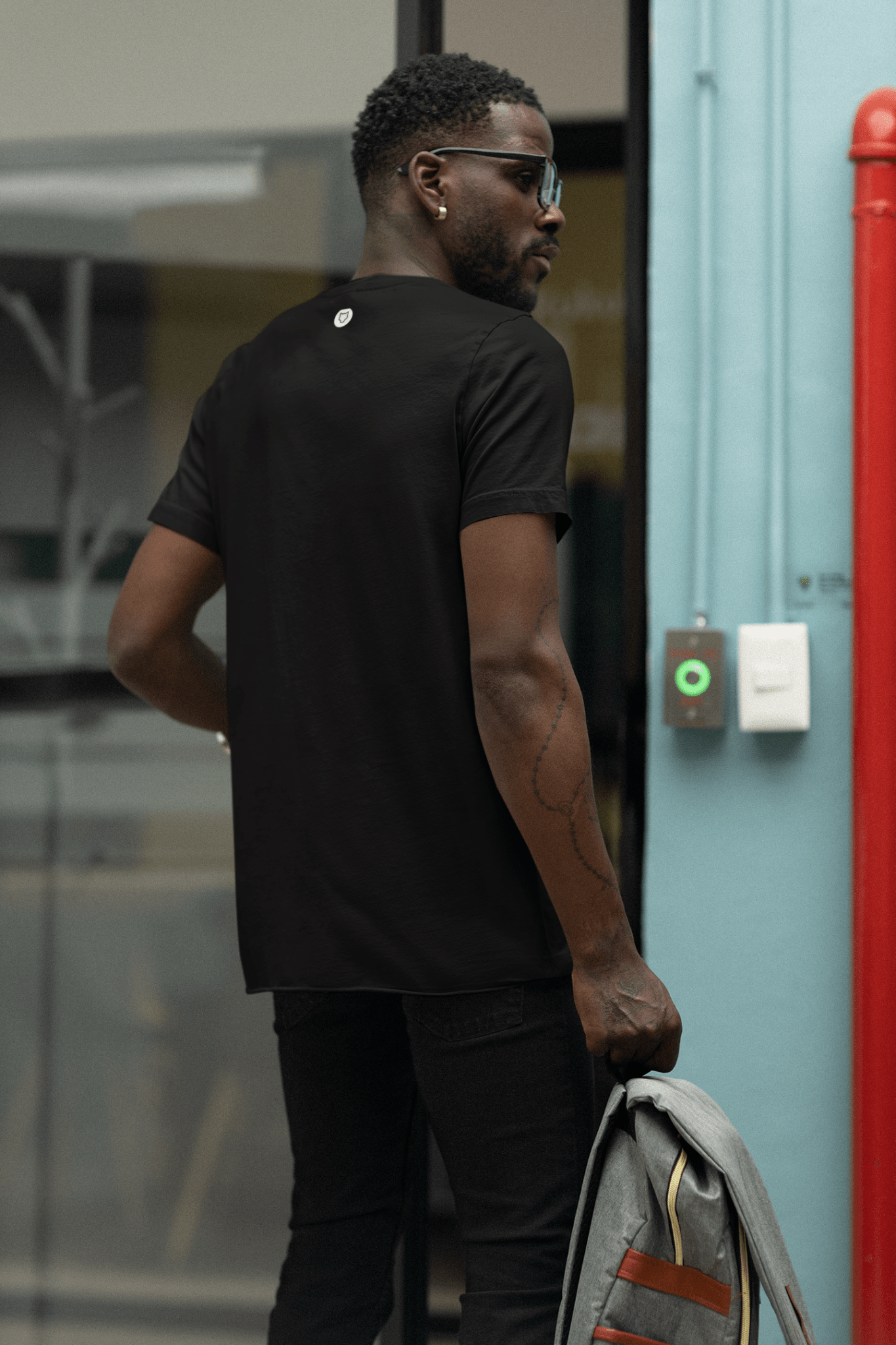Black Casual T-shirt by Forge Athletica worn by a black man posing his back. The man is carrying a cool bag and wearing a pair of sunglasses and black jeans.