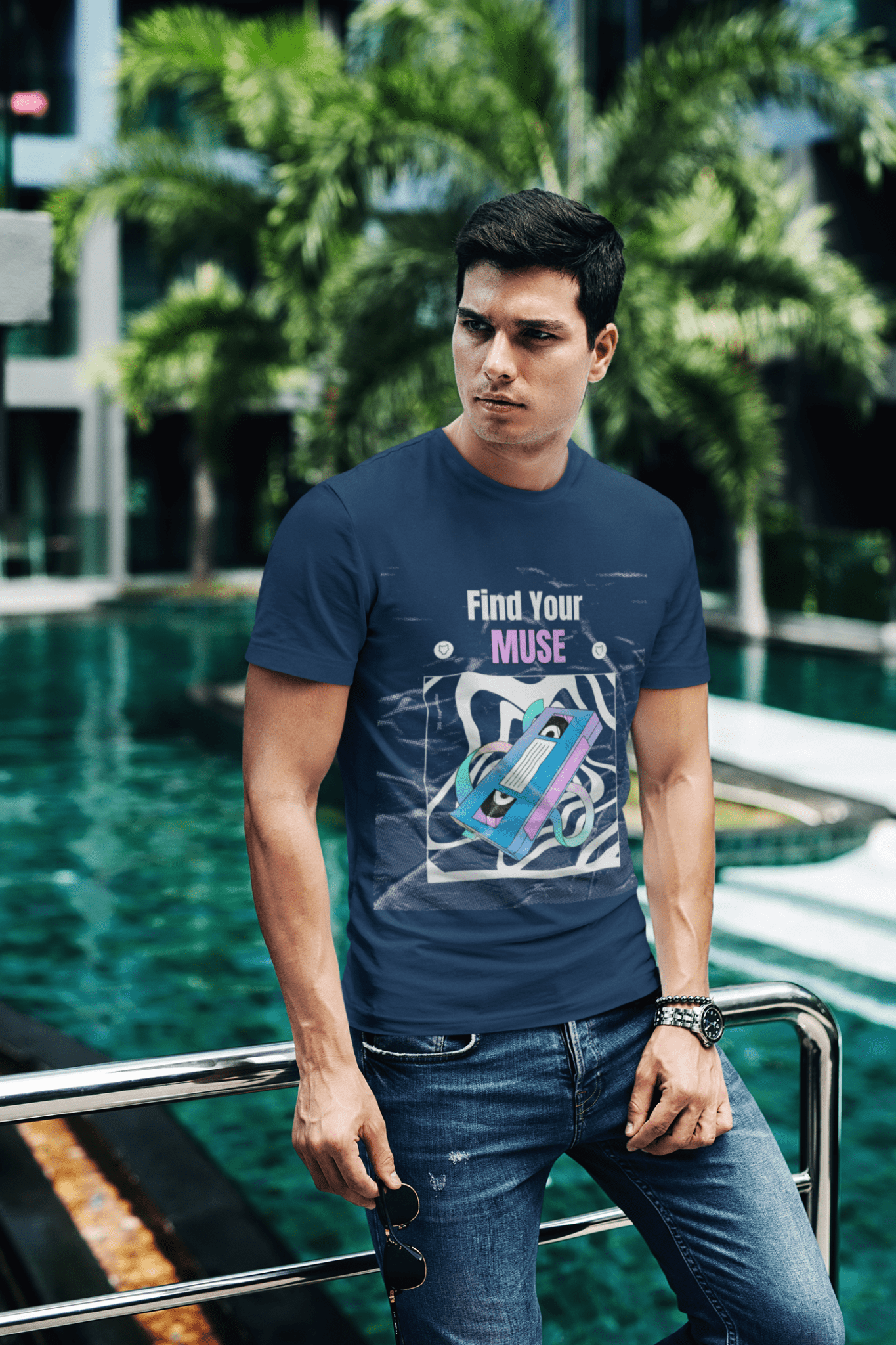 Man Posing in a Navy Blue Round Neck T-Shirt in front of a swimming Pool with a watch in one hand.